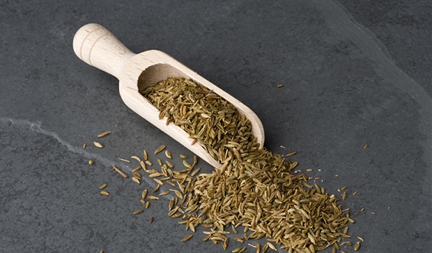 Cumin seeds in a wooden scoop.